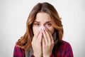 Close up portrait of beautiful woman sneezes and coughs, uses tissue, rubs nose, has bad cold, over white background. Low