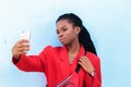 Close up portrait of a beautiful young african american woman with pigtails hairstyle in red business suit taking selfie using Royalty Free Stock Photo