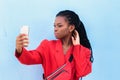 Close up portrait of a beautiful young african american woman with pigtails hairstyle in red business suit taking selfie using Royalty Free Stock Photo