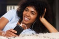 Close up beautiful young african woman lying on floor listening to music with earphones and mobile phone Royalty Free Stock Photo