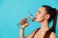 beautiful young brunette woman in sportswear drinks water from a bottle on a blue background, space for text Royalty Free Stock Photo