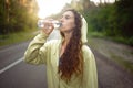 Beautiful young Caucasian girl  standing on asphalt forest road Drinks water from plastic bottle after jogging Royalty Free Stock Photo