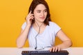 Close up portrait of beautiful young dark haired girl in headphones with microphone, working on keyboard and talking with somebody Royalty Free Stock Photo