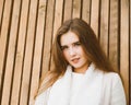 Close up portrait of beautiful young girl with long brown hair on wooden background of planks, winter or autumn outdoor photoshoot Royalty Free Stock Photo