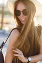 Close-up portrait of a beautiful young girl with long dark hair wearing straw hat, dark sunglasses and black backpack Royalty Free Stock Photo