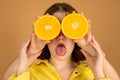 Close-up portrait of a beautiful young girl, two pairs of hands holding half of oranges close to her face isolated over