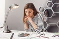 Close up portrait of beautiful young serious female architect student with brown hair in striped look, holding head with