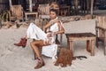 Close up portrait of beautiful young stylish boho woman sitting on wooden chair on the beach at sunset Royalty Free Stock Photo