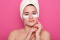 Close up portrait of beautiful young woman with collagen pads under her eyes, stands wearing white towel on head, charming gentle Royalty Free Stock Photo