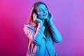 Close up portrait of beautiful young woman in headphones listening to music. Happy smiling girl wearing leather pink jacket Royalty Free Stock Photo