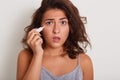 Close up portrait of beautiful young woman holding eye drops, brunette afraids of using medicine, model looking at camera with