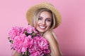 Close-up portrait of beautiful young woman in straw hat holding peonies bouquet over pink background Royalty Free Stock Photo