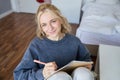 Close up portrait of beautiful young woman, writing in her diary, journal or planner, sitting in a room, smiling and Royalty Free Stock Photo