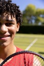 Close-up portrait of biracial young man with tennis racket smiling in tennis court on sunny day Royalty Free Stock Photo