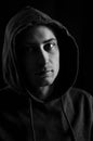 Close up portrait in black and white of a young man with a hood on his head looking grumpy in a dark atmosphere Royalty Free Stock Photo