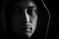 Close up portrait in black and white of a young man with a hood on his head looking grumpy in a dark atmosphere Royalty Free Stock Photo