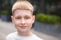 close up portrait of blond boy with blue eyes looking at camera and walking outdoors in city street Royalty Free Stock Photo