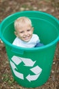 A little cute blond boy sitting in a green recycling bin on a blurred park ground background. Ecology pollution concept. Royalty Free Stock Photo