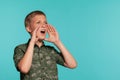 Close-up portrait of a blonde teenage boy in a green shirt with palm print posing against a blue studio background Royalty Free Stock Photo