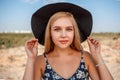 A close-up portrait of a blue-eyed blonde girl in a black hat and a floral print dress.she`s posing in a vineyard during sunset Royalty Free Stock Photo