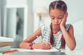 Close-up portrait of bored cute Afro-American girl doing writing homework.