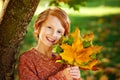 Close-up portrait of a boy with maple leaves in a sunny autumn park. A child holds a bouquet of fallen leaves near a tree Royalty Free Stock Photo