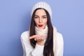 Close up portrait of brunette young female blowing air kiss to camera, expresses her affection, dresses white warm clothing, has Royalty Free Stock Photo