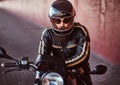 Close-up portrait of a brutal bearded biker in helmet and sunglasses dressed in a black leather jacket sitting on a Royalty Free Stock Photo