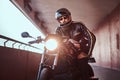 Close-up portrait of a brutal bearded biker in helmet and sunglasses dressed in a black leather jacket sitting on a Royalty Free Stock Photo