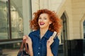 Close up portrait business woman with credit card smiling looking at camera you red lips  curly hair isolated outdoors near store Royalty Free Stock Photo