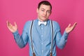 Close up portrait of careless guy spreading hands in helpless gesture, young man wearing blue shirt, suspenders and white bowtie Royalty Free Stock Photo