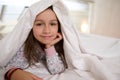 Close-up portrait of a Caucasian beautiful little kid girl lying on the bed under white duvet, smiling looking at camera Royalty Free Stock Photo