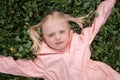 Close up portrait of Caucasian blonde girl with two ponytails in pink jacket on green grass. Towheaded small girl outside Royalty Free Stock Photo