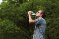 Handsome young sportsman drinking water out of bottle after running workout at public park. Taking break after hard workout