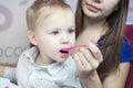 Close-up portrait of a caucasian kid boy with a big blue eyes, which his mother with a spoon is feeding ice cream in a cafe Royalty Free Stock Photo