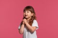 Close-up portrait of a little brunette girl dressed in a white t-shirt posing against a pink studio background. Sincere Royalty Free Stock Photo