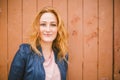 Close-up portrait of charming redhead caucasian young woman with cute freckles cheerfully while standing over on a wooden wall. Royalty Free Stock Photo