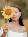 Close up portrait of charming woman holding sunflower. One eye is covered by sunflower. Focus on flower. Blurred face Royalty Free Stock Photo