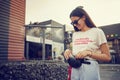 Portrait of a girl in dark sunglasses posing near a city mall. Dressed in white t-shirt, blue trousers, black waist bag Royalty Free Stock Photo