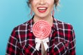 Close-up portrait of a charming young pin-up woman in a plaid shirt with a big lollipop against a blue background Royalty Free Stock Photo