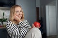 Close-up portrait of charming young smiling blonde who enjoys comfort of home and holds juicy red apple in her hands.