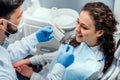 Close up portrait of charming young woman sitting in dental chair while stomatologist selecting color tone of her teeth