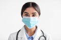 Close up portrait of cheerful pretty young indian lady doctor in white coat with stethoscope in protective mask Royalty Free Stock Photo