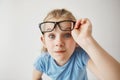 Close up portrait of cheerful small girl with blonde hair and blue eyes funny imitates adult person with glasses with Royalty Free Stock Photo
