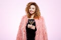 Close up portrait of cheerful smiling beautiful brunette curly girl in pink fur coat holding cocktail glass over white Royalty Free Stock Photo