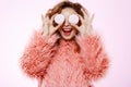 Close up portrait of cheerful smiling beautiful brunette curly girl in pink fur coat holding marshmallow over white Royalty Free Stock Photo