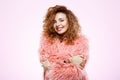 Close up portrait of cheerful smiling beautiful brunette curly girl in pink fur coat over white background. Royalty Free Stock Photo
