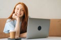 Close-up portrait of cheerful young beautiful woman sitting at desk with laptop and cup with hot coffee at cozy cafe Royalty Free Stock Photo