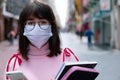 Portrait of college girl walking in the city center. Woman wearing face mask with cellphone in hands and carrying school