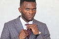 Close up portrait of confident handsome african business man in modern grey suit straightening his tie against a gray Royalty Free Stock Photo